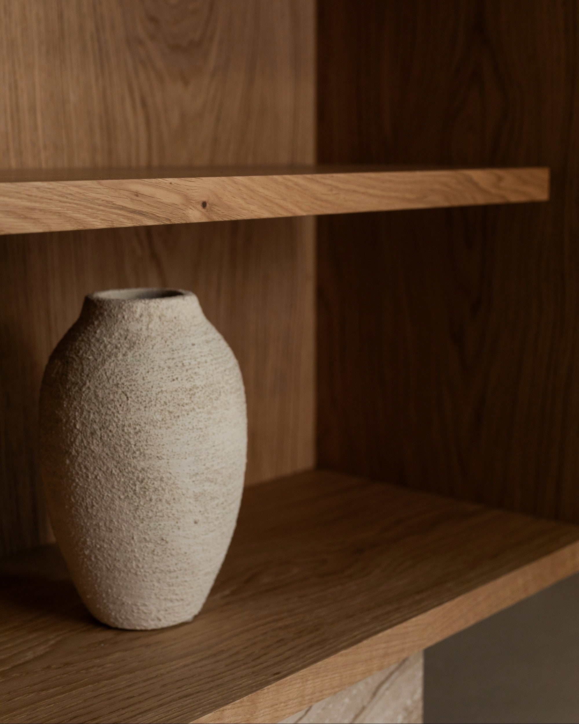 A textured, light-colored ceramic vase decorates the BLOCK Sideboard by un'common, surrounded by elegant furniture and warm natural wood tones in a minimalist space.