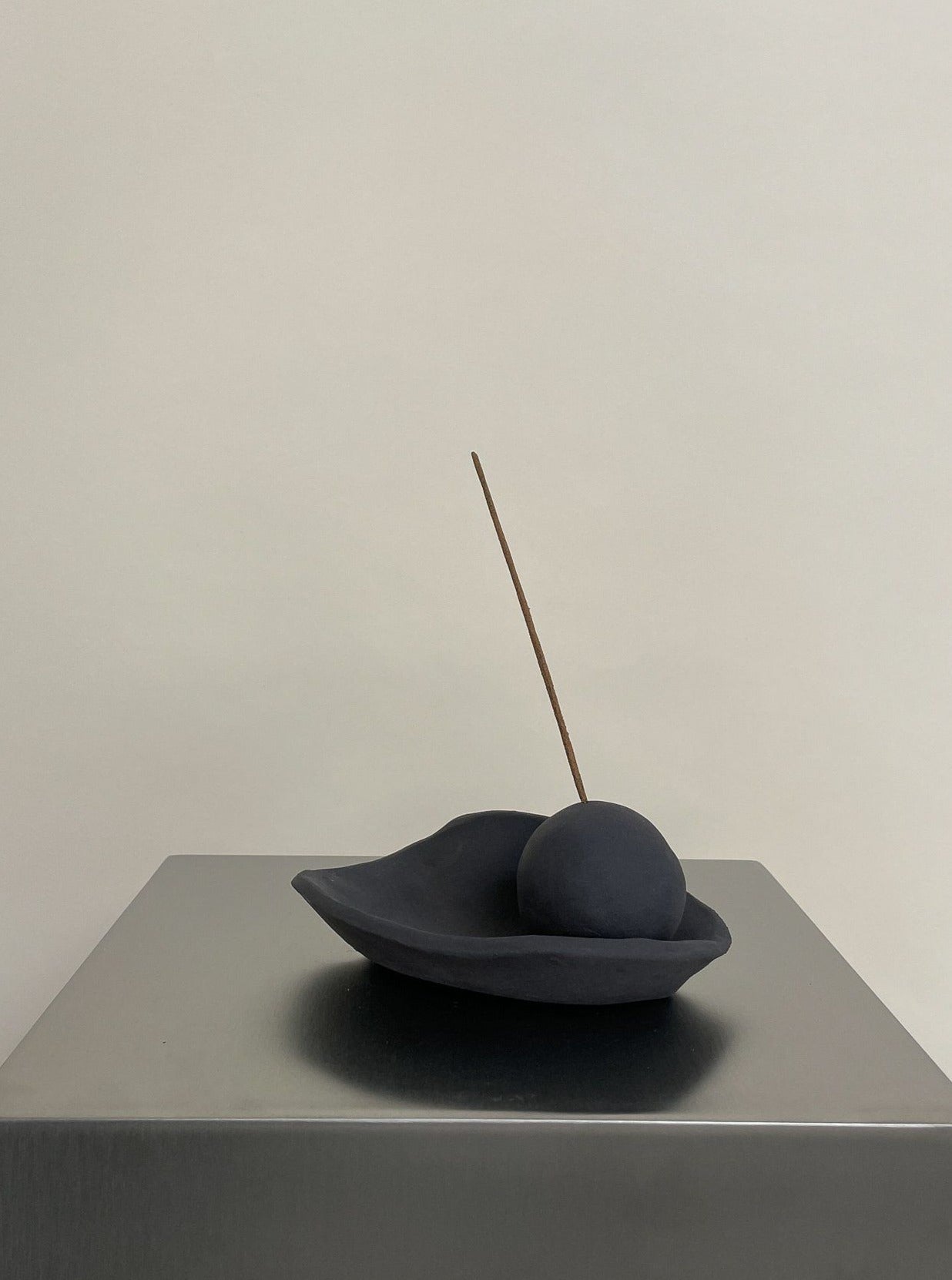 The 2222Studio Incense Holder in black stoneware features a minimalist curved dish with a sphere, holding one incense stick and adding modern elegance to your home decor.