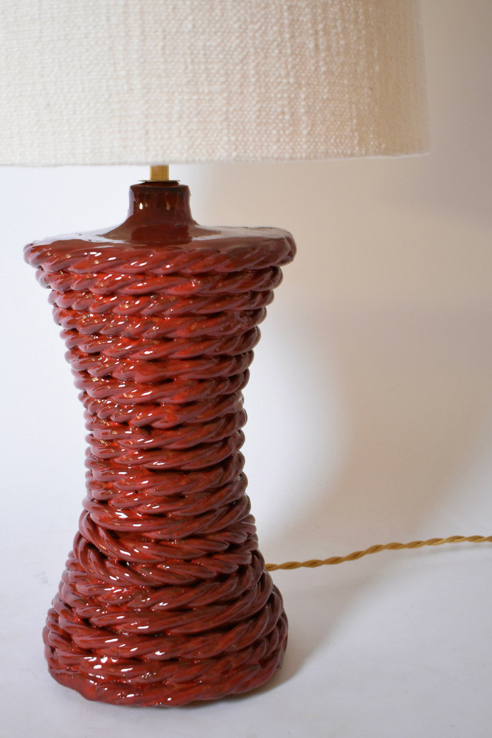 The "Kasaï" Red Ceramic Table Lamp by Barracuda Interiors features a glossy, twisted rope-like base and a large, textured off-white lampshade with a visible cord—an eye-catching accent for any interior.