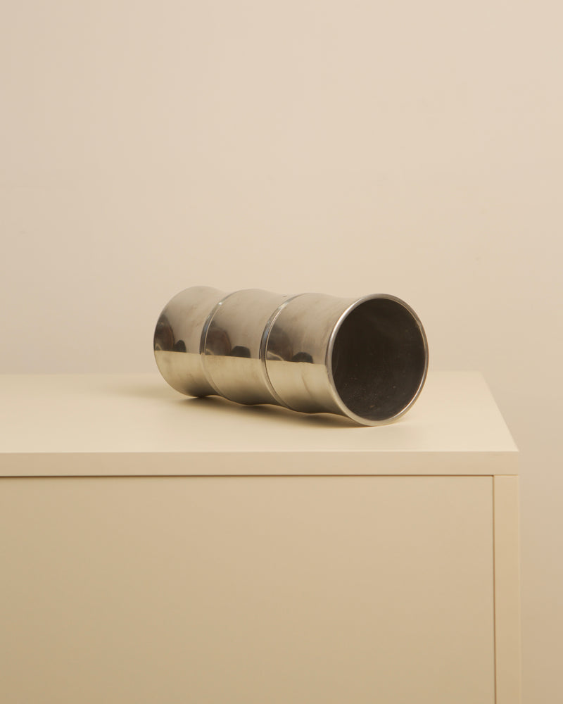 Polished cast aluminum cylindrical vase lying on beige surface
