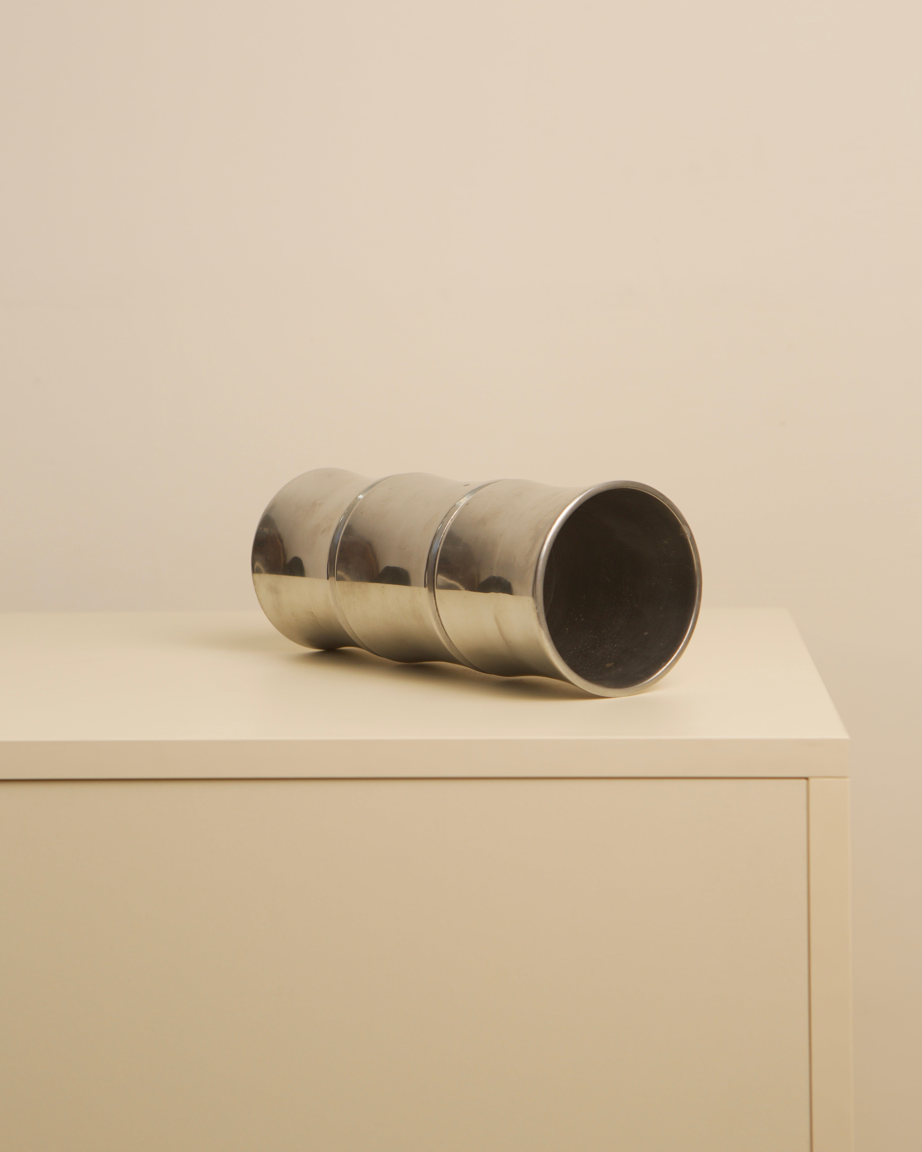 Polished cast aluminum cylindrical vase lying on beige surface