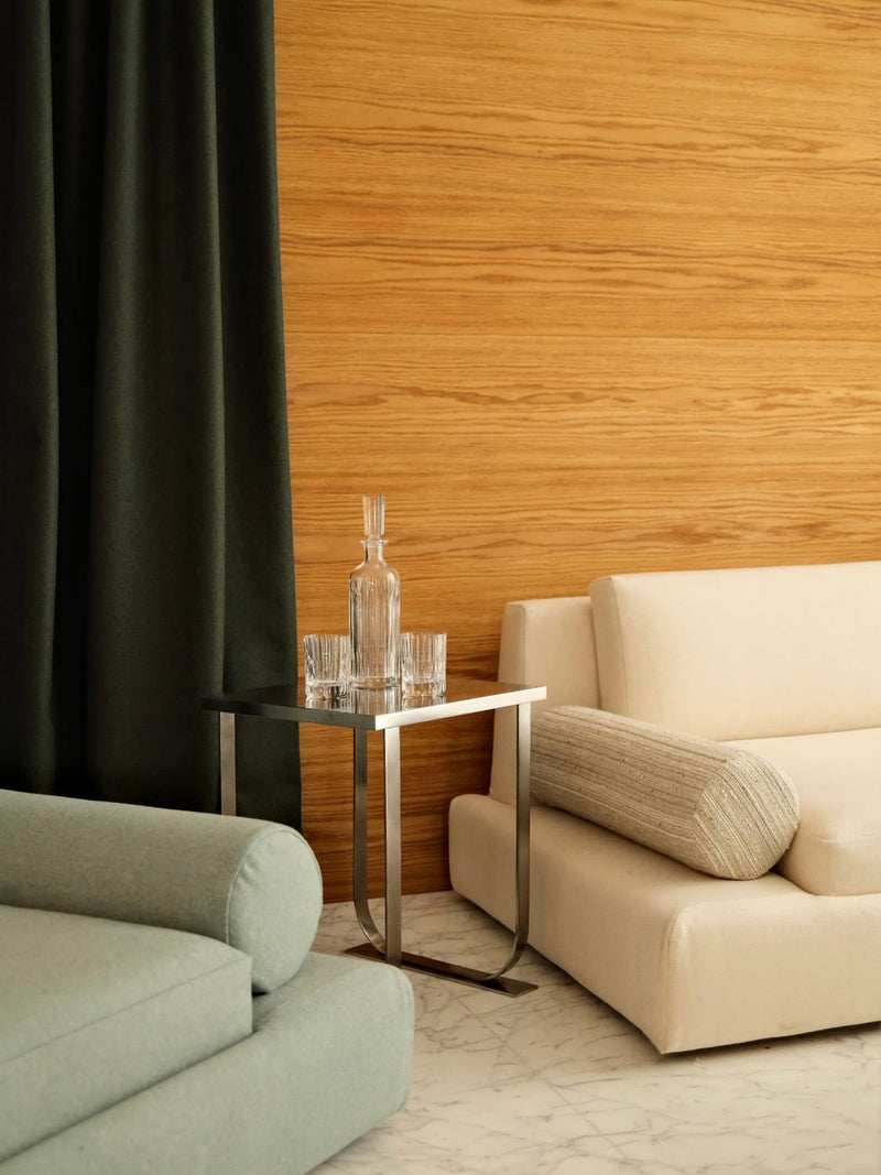 Serge Side Table, stainless steel — angled view beside modern sofa