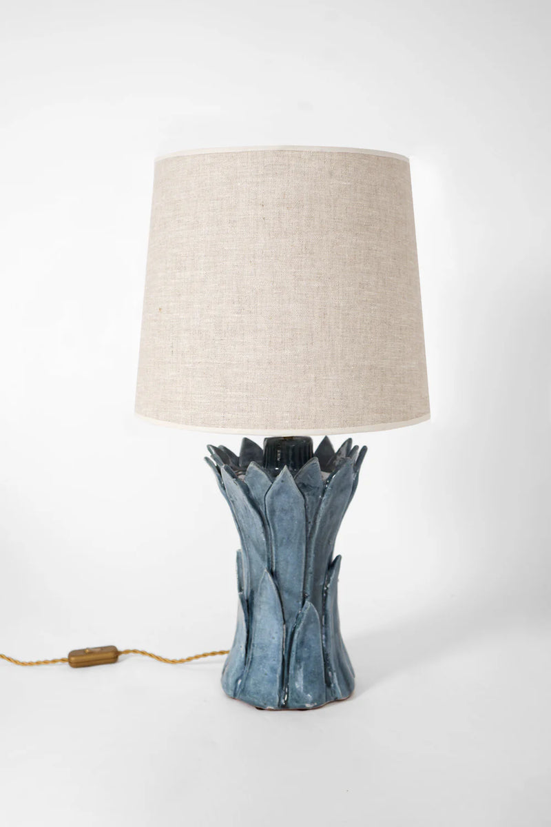 The "Sintra" Blue Table Lamp by Barracuda Interiors features a beige fabric shade, a blue terracotta base with a leaf-like design, and a visible gold cord and switch. Made in Portugal, it's shown on a plain white background.