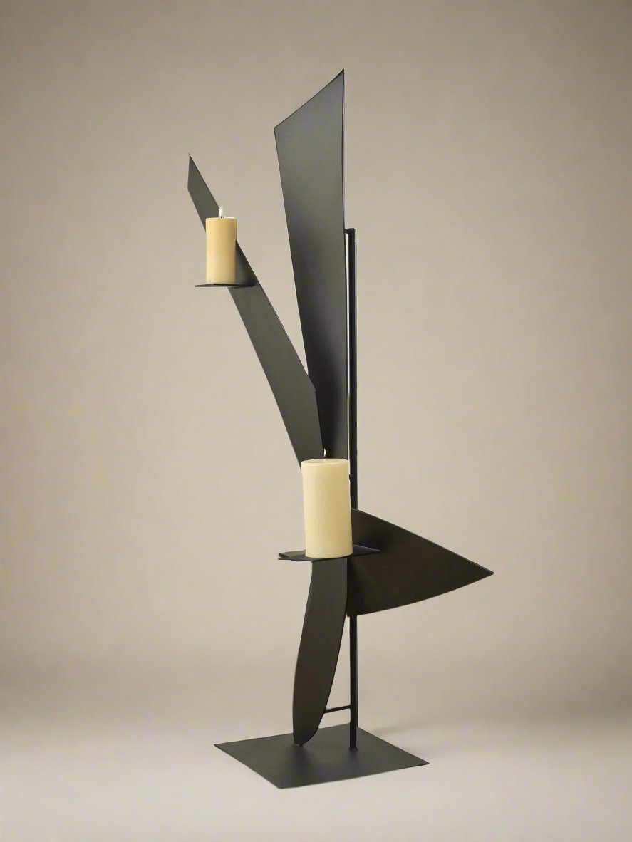 Animate Objects’ Bird Candleholder features a modern, abstract black powder coat design with geometric shapes and two beige pillar candles on separate platforms, showcased against a plain beige background.