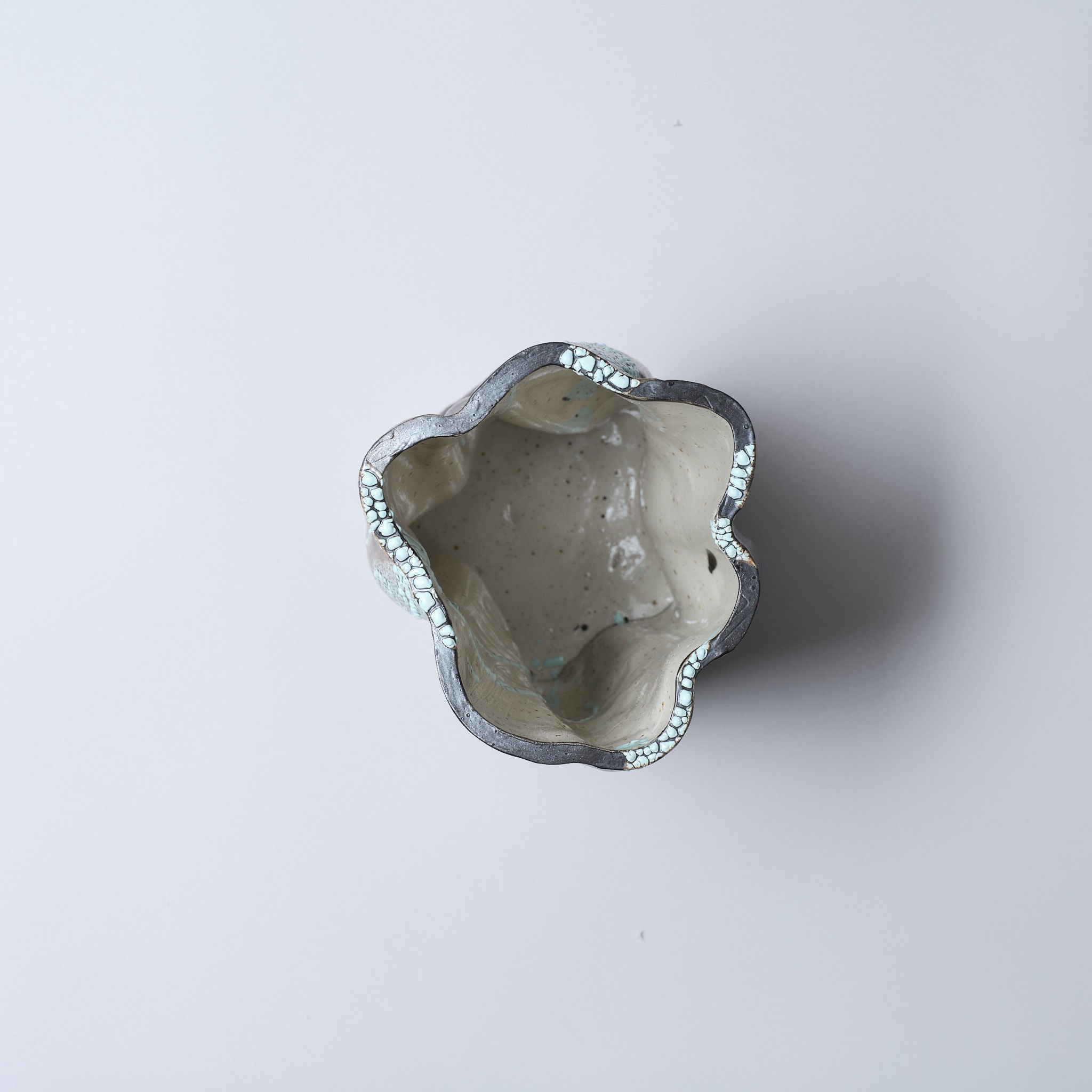 A top-down view of the Astrid Öhman Swirly Vase Brown and Light Blue, a handmade stoneware ceramic vase with an irregular wavy rim and glossy light gray interior, set against a plain white background.