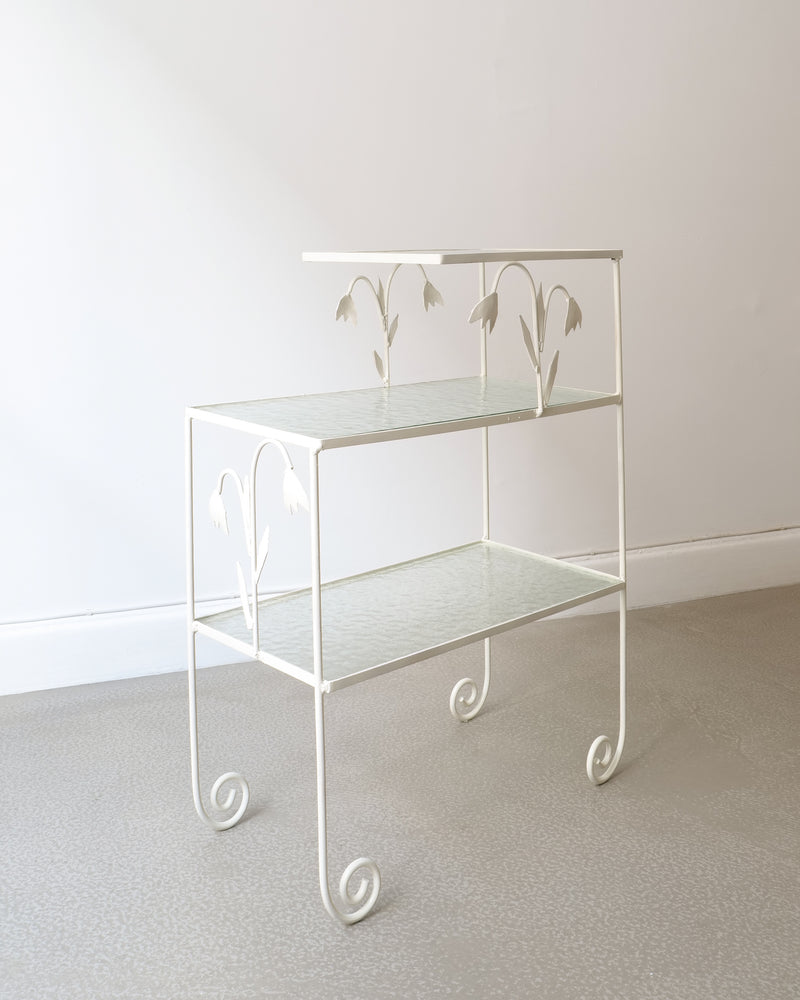 White metal tiered side table with floral cutouts and glass shelves