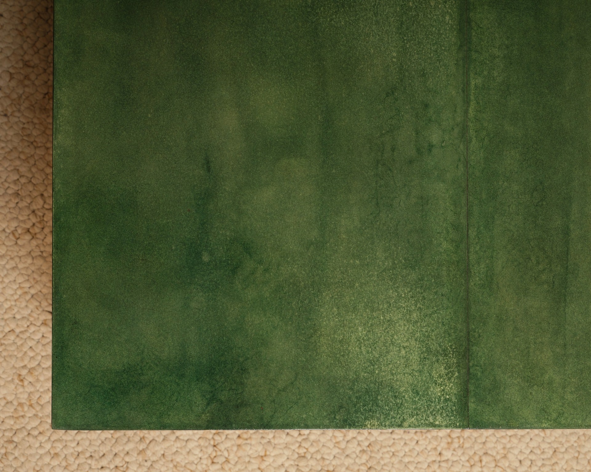 The Green Parchment Table by Galerie Vauvart features a surface with Aldo Tura-style green parchment, displaying subtle color variations, atop a beige, textured carpet-like base composed of small rounded shapes.