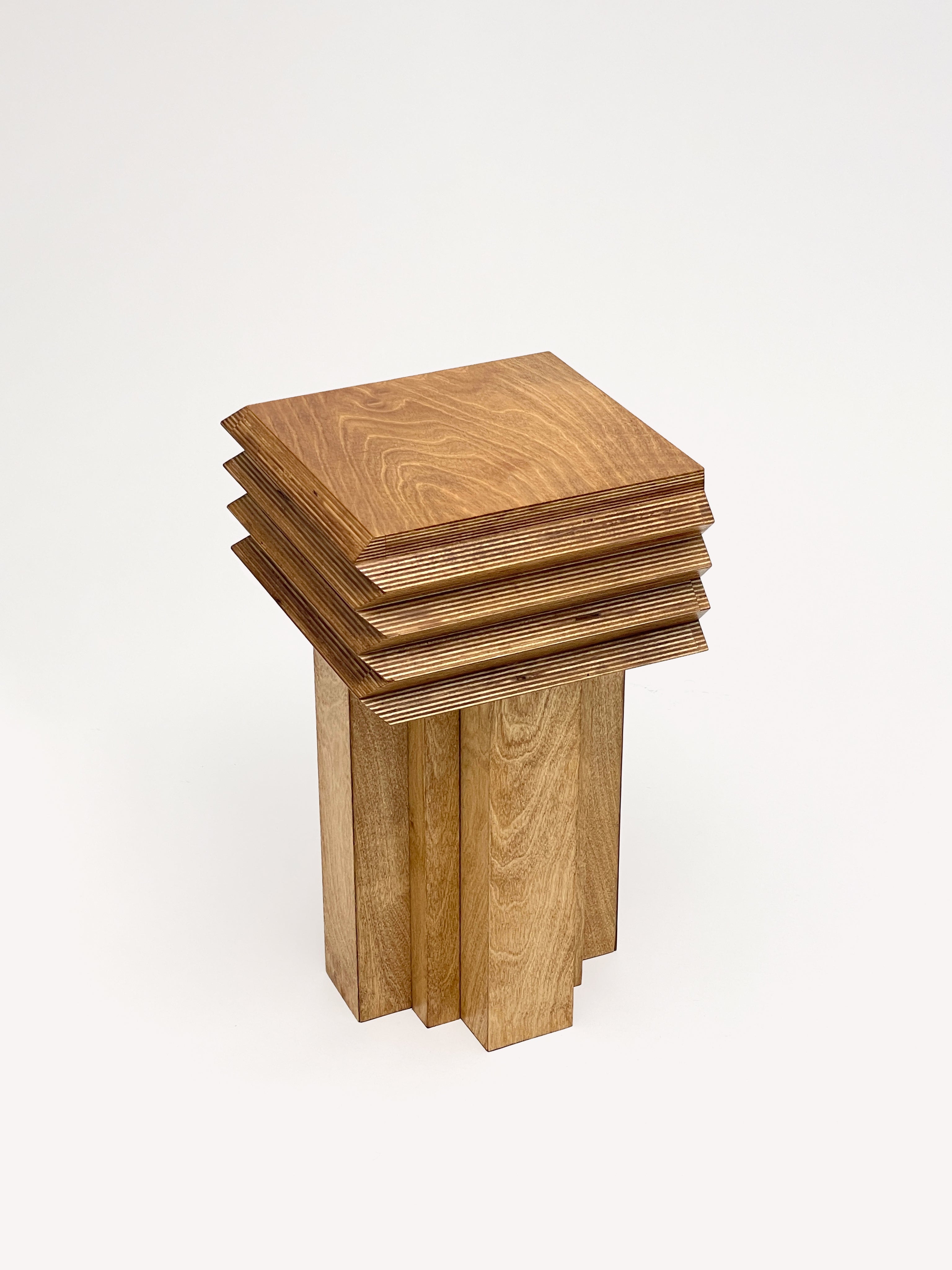 The MM Stool - Butterscotch by GOONS is a modern wooden stool with a square, layered seat and staggered legs, crafted by GOONS. Shown on a white background, it's ideal for anyone looking for customizable furniture.