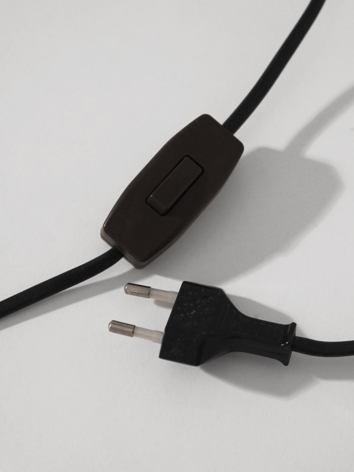 A black cord with a European two-pin plug and inline switch lies on a white surface, ideal for pairing with the Vintage Stories Mid-Century Swedish Wood And Iron Tall Lamp in stylish lighting setups.