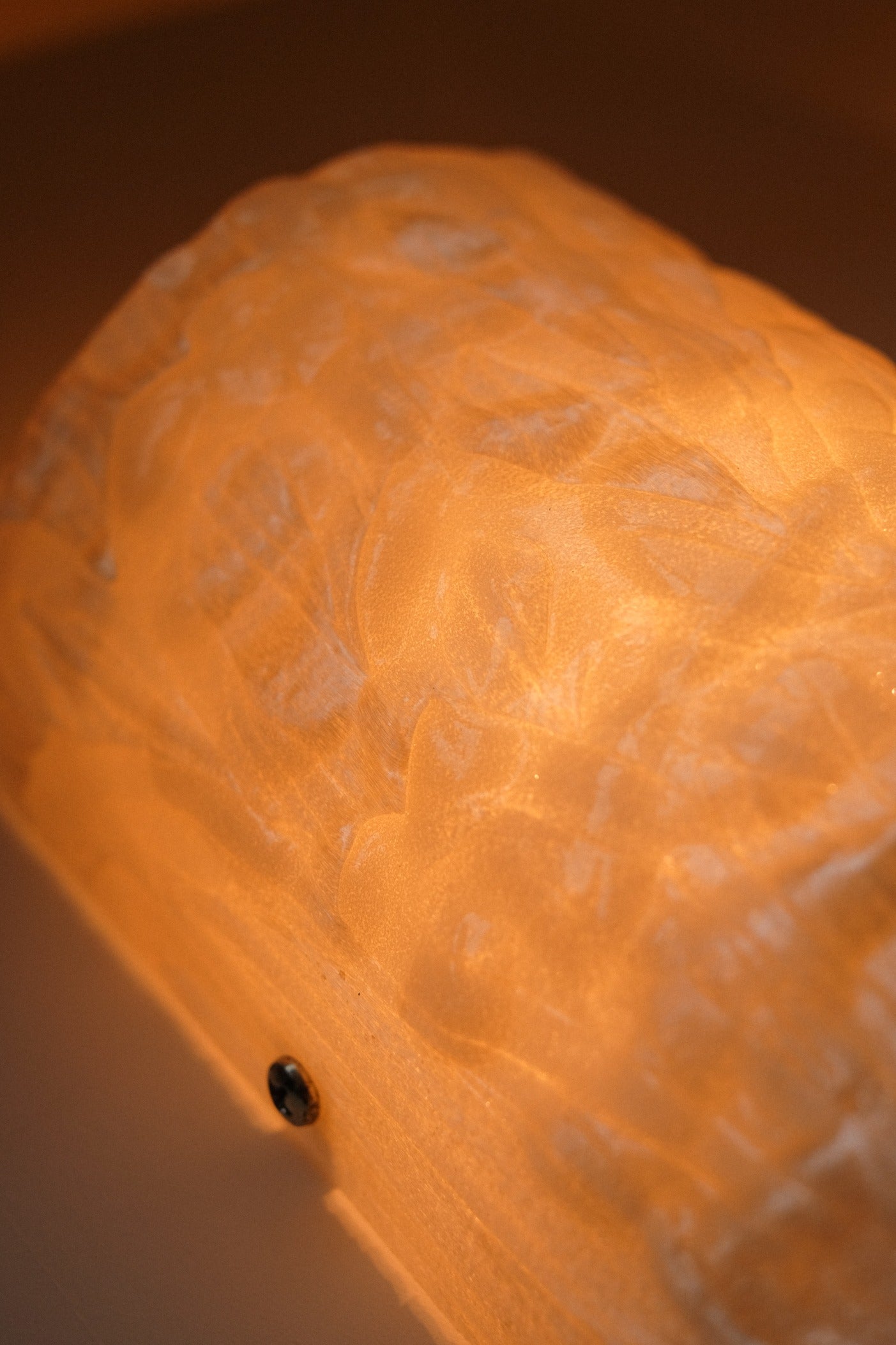 Close-up of a softly glowing Set of 2 Mother-of-pearl Wall Lamps by septembre studios, featuring a textured surface and warm orange light that gently diffuses to evoke the classic 1980s vintage wall lamp style.