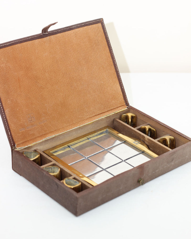 Brutalist Tic Tac Toe — close-up of brass game pieces in box