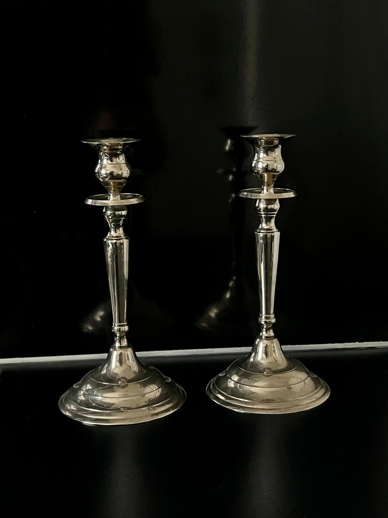 Pair of polished silver candlesticks with tapered stems on dark surface