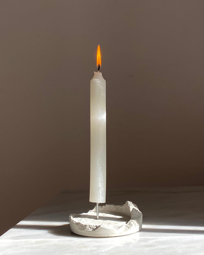 Lotus cement candle holder with lit white candle on beige surface
