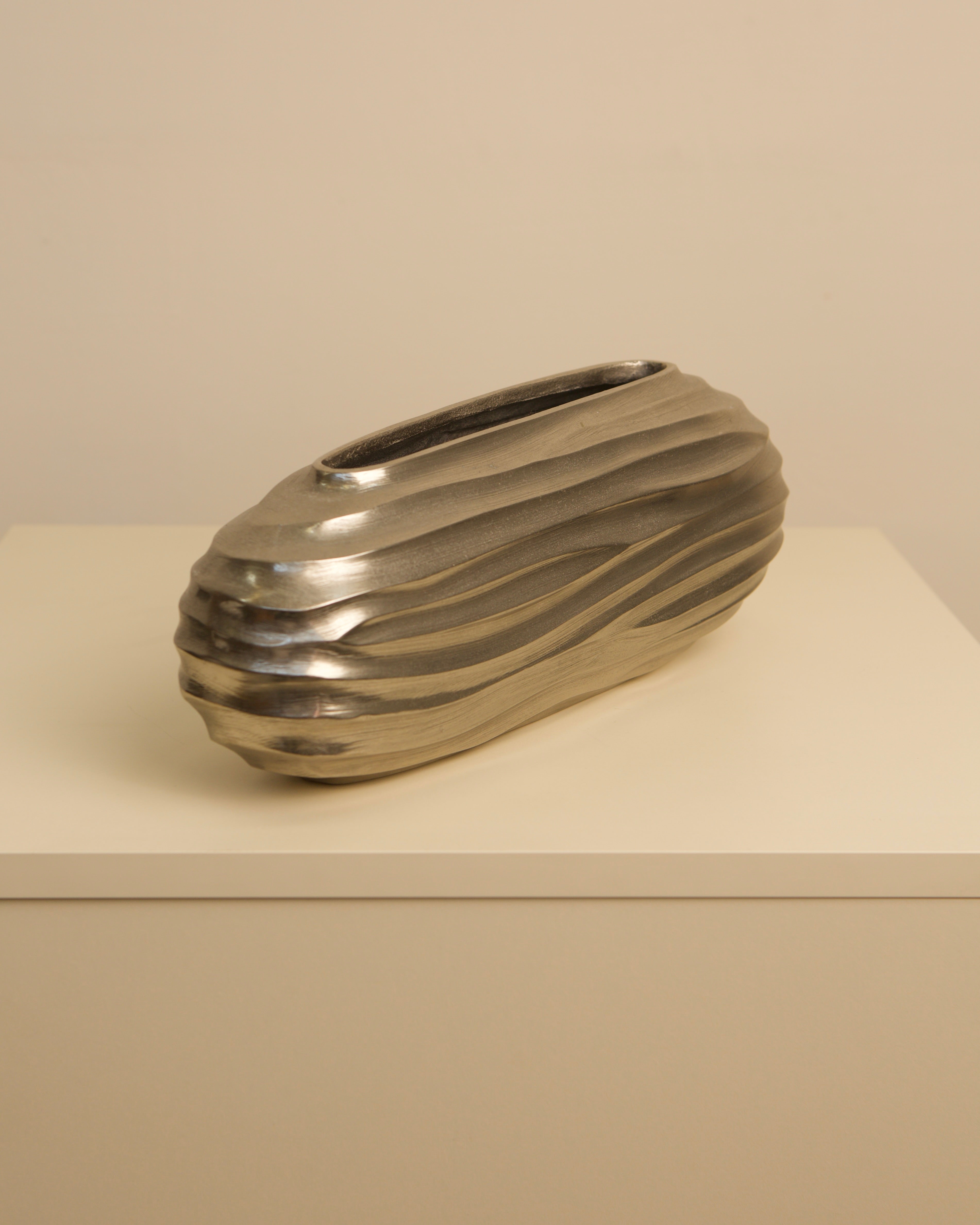 Cast aluminum strillé vase with ribbed surface on beige shelf