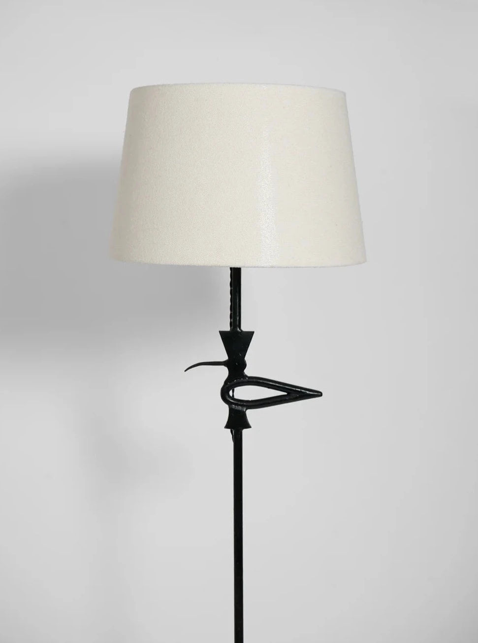 The "Brejos" Floor Lamp by Barracuda Interiors features a black wrought iron stand, white shade, and decorative bird detail below the shade, set against a light gray background—providing customizable lighting for your space.