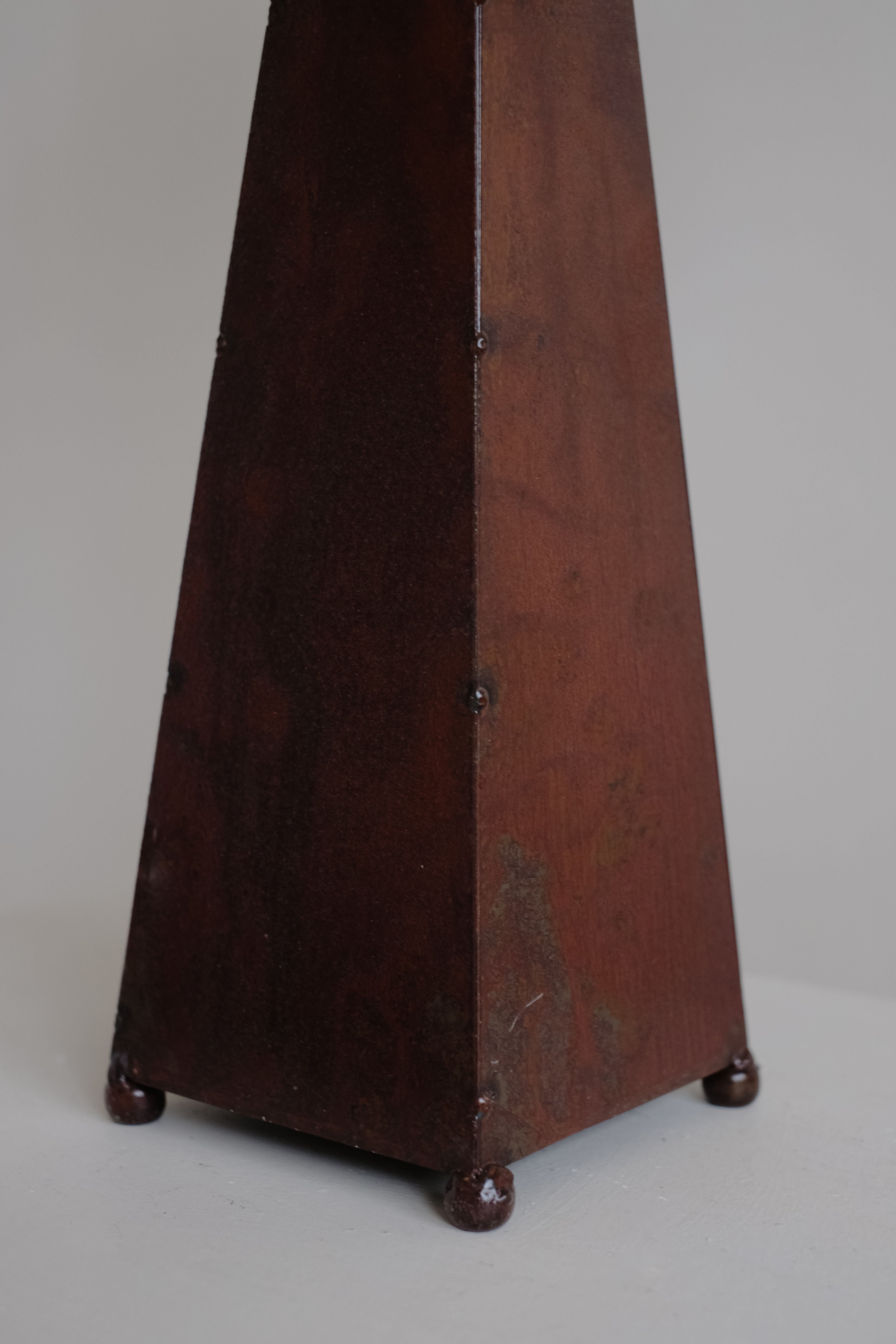 A close-up of the lower section of the septembre studios Obelisk Table Lamp highlights its dark reddish-brown, four-sided wooden base with visible screws at the edges and small round feet at each corner.