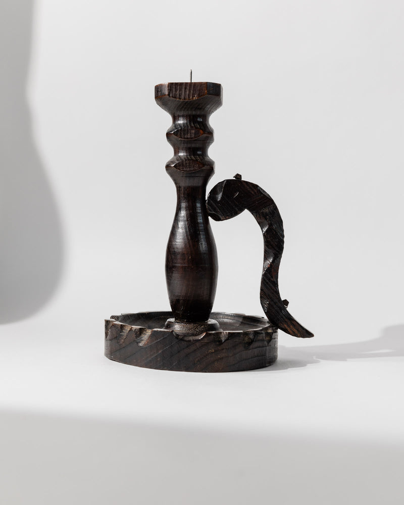 The 1960s Wooden Candleholder in Handcarved Dark Wood by Bottega Jacobs features a carved handle, round base, and subtle Brutalist design, all showcased in its dark finish against a plain white background.