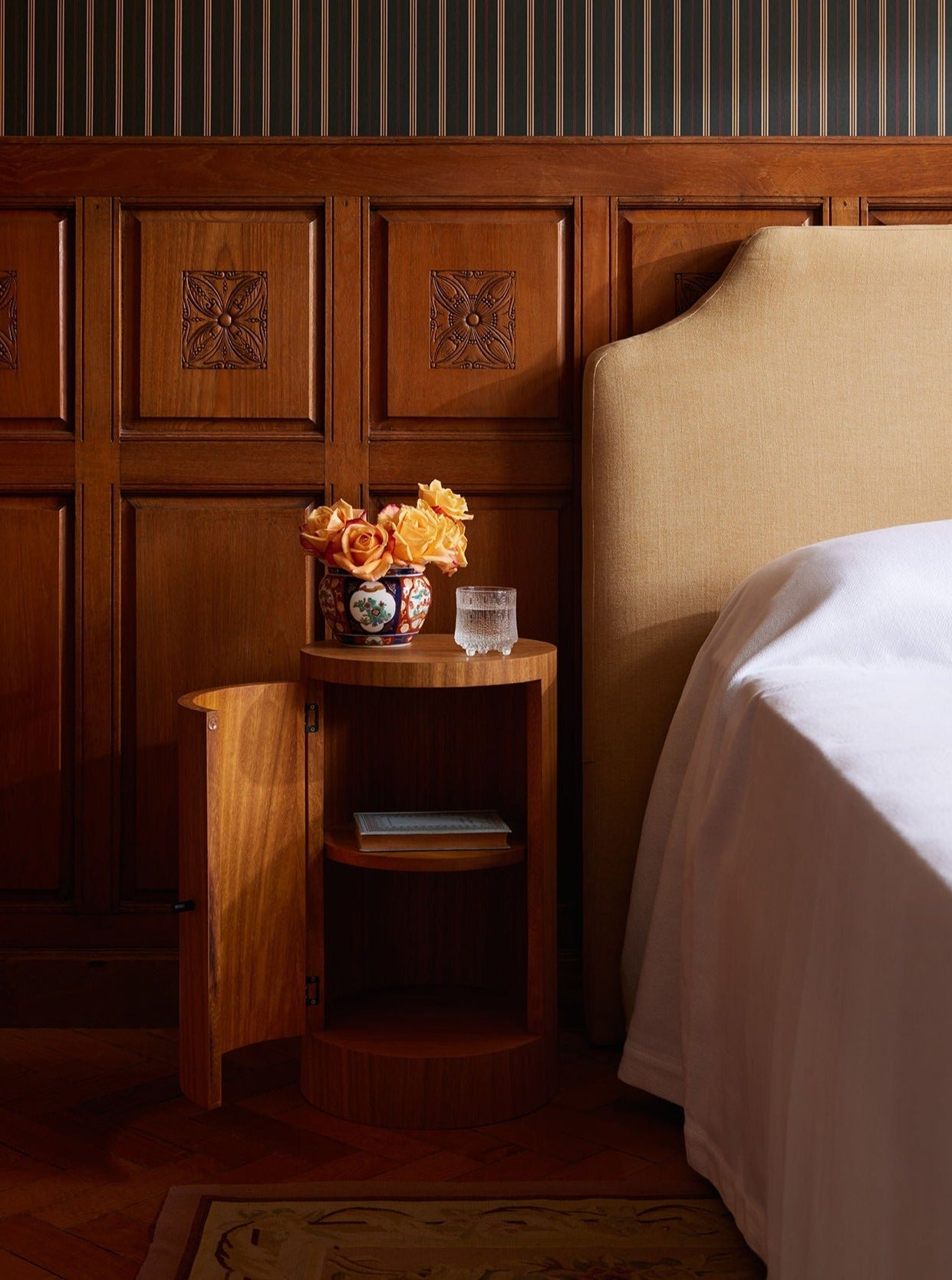 Pair of Constant Nightstand in Oiled Iroko — close-up of round nightstand with floral arrangement