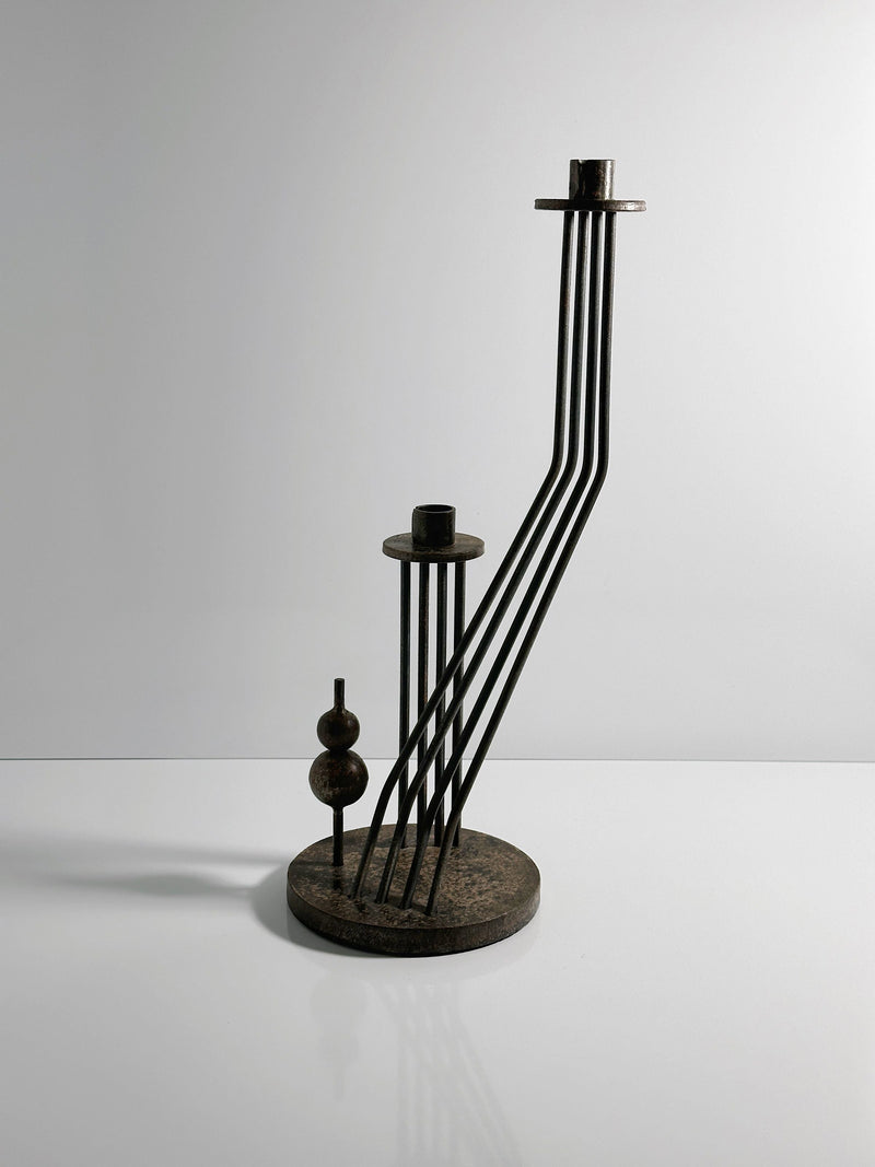 The Solid Brutalist Metal Candleholder by Dodo Vintage (1960s) features vertical and angled rods with circular and spherical details on a round base, showcasing a striking brutalist design against a light background.