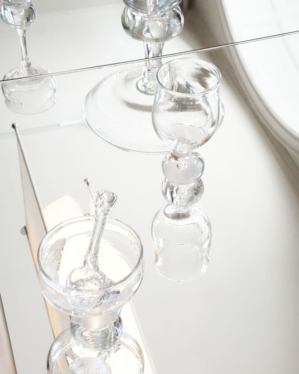 Clear glass stemware set with decorative bulbous stems on white surface