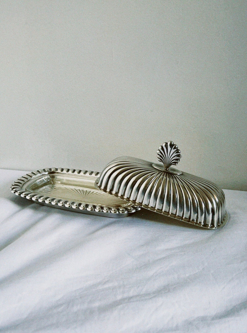 Silver shell-detailed butter dish with fluted dome lid on marble
