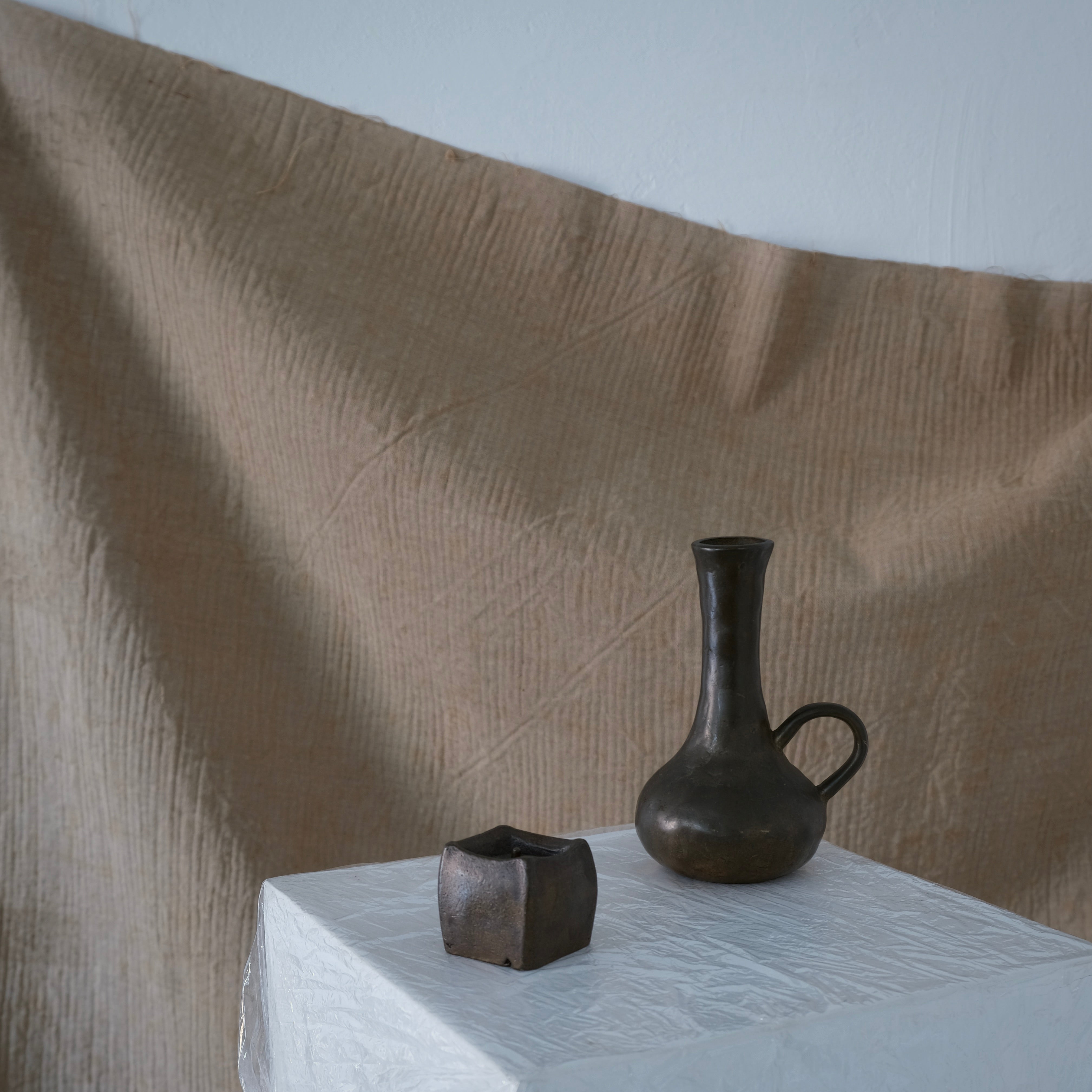 Brutalist Cast Bronze Candle Holder & Vase Set, 1970s — textured bronze vase and holder on white pedestal