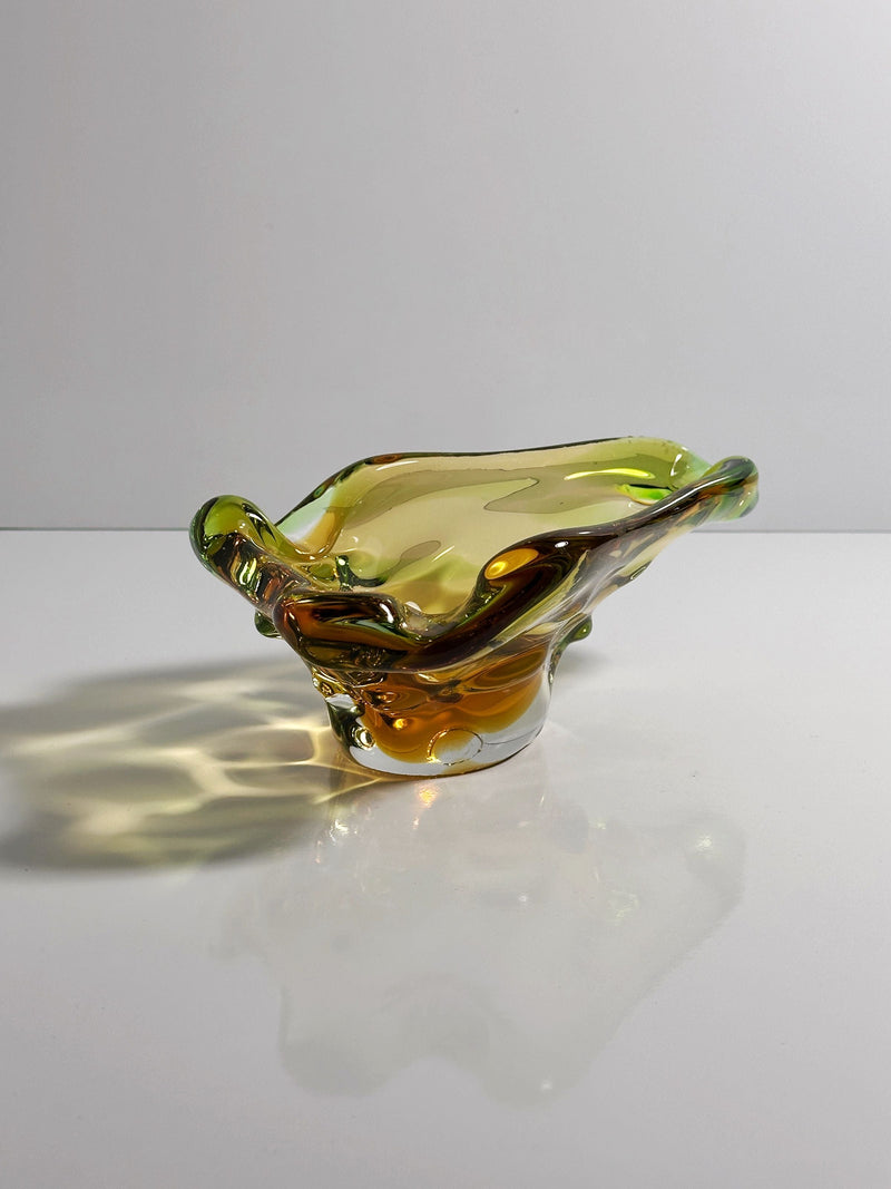 The Bohemian Vide-poche from the 1960s by Dodo Vintage features exquisite craftsmanship, its wavy amber and green glass casting colorful shadows—a stunning example of mid-century design.