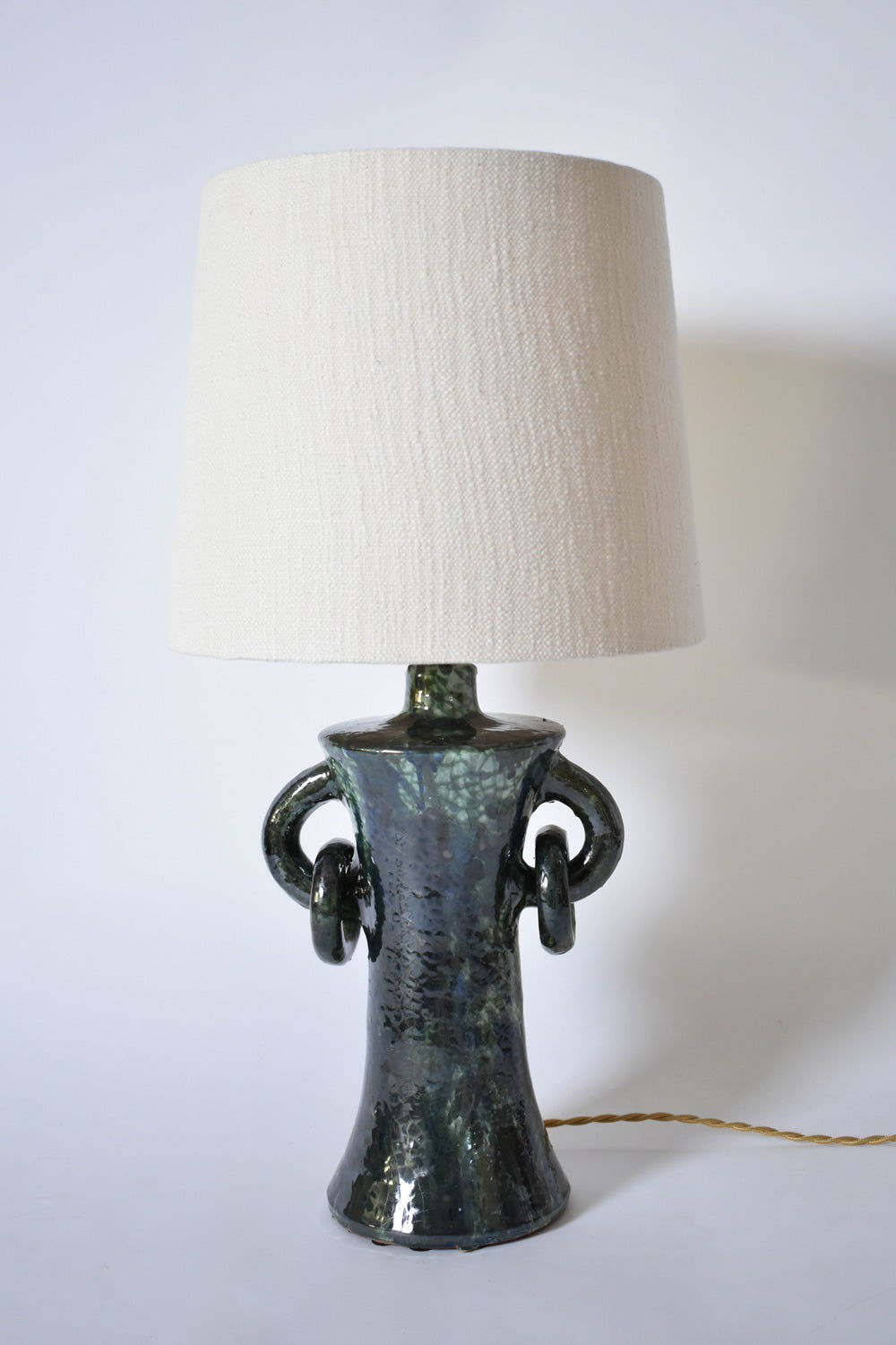 The "Kasaï" Blue & Green Ceramic Lamp by Barracuda Interiors features a textured, glossy base with two looped handles, a large off-white fabric shade, and a twisted gold cord. Made in Portugal.