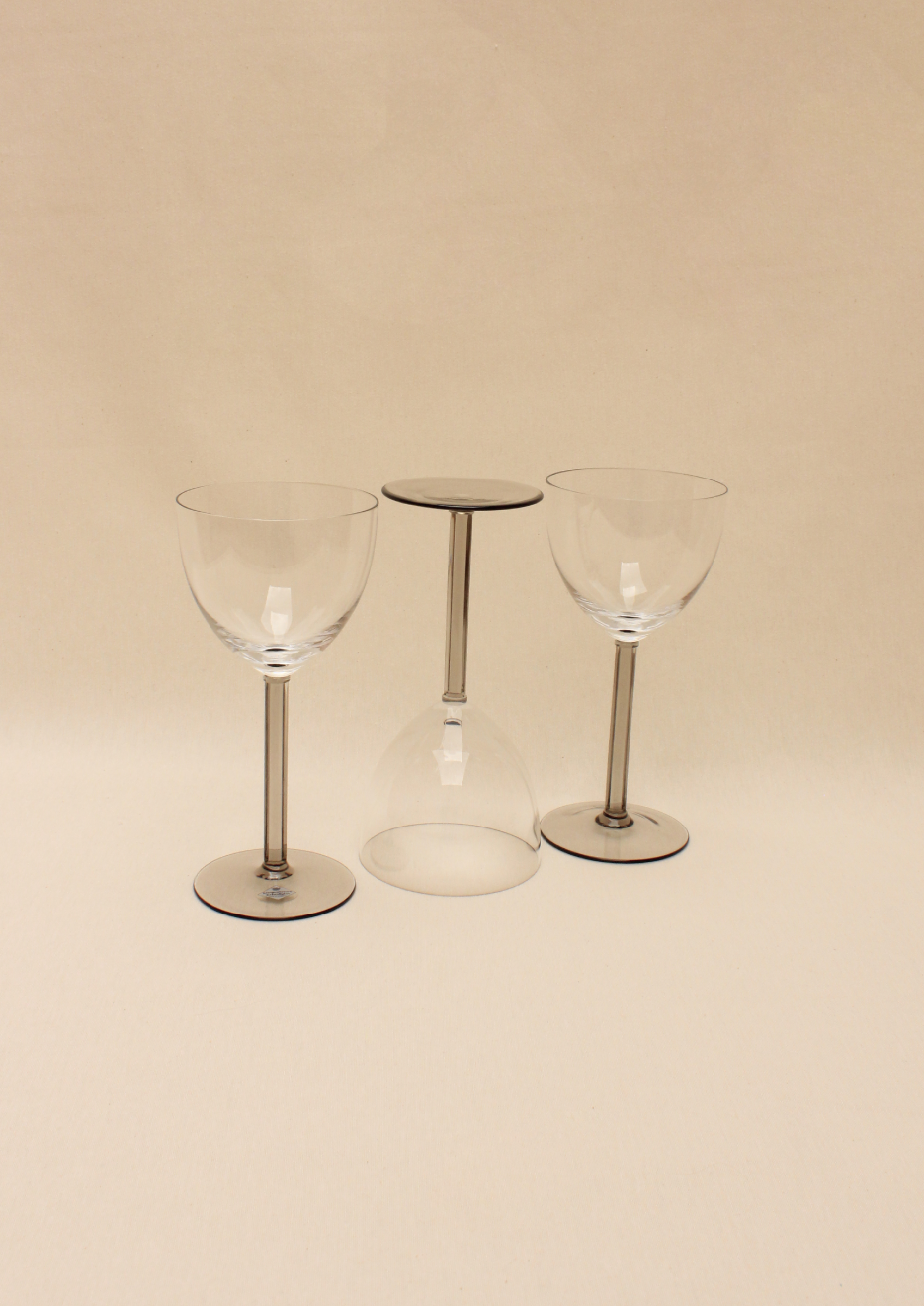 Three Boga Avante Shop Crystal Wine Glasses arranged symmetrically on a beige background, with the middle glass inverted and balanced on its rim between the other two.