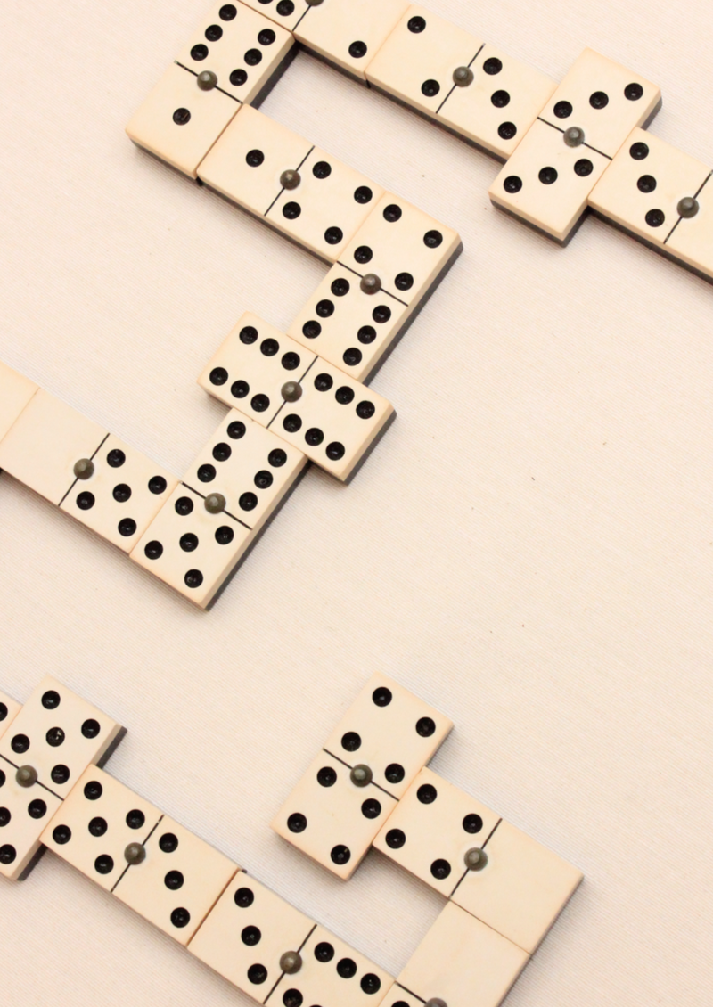 A setup of Chamelot Dominoes with black dots on a beige surface, arranged in an interconnected pattern during a game purchased from Boga Avante Shop.