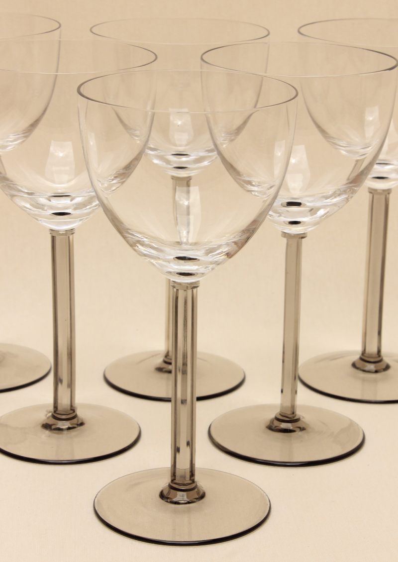 The Crystal Wine Glass Set by Boga Avante Shop features a collection of handcrafted wine glasses with long stems arranged in rows on a light surface, showcasing reflections and transparency that enhance any luxury interior.