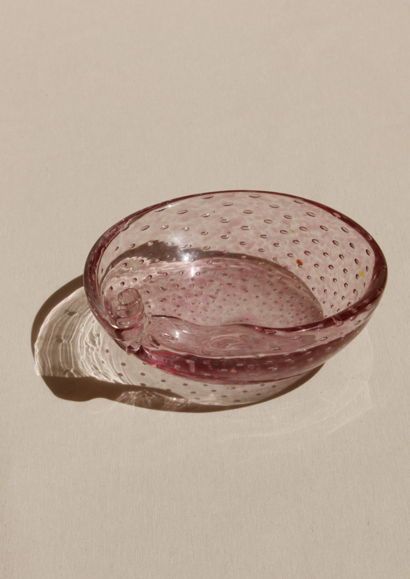 A pink Boga Avante Shop Bullicante Murano Bowl, with a bubble texture, photographed on a beige background with a shadow cast by sunlight.
