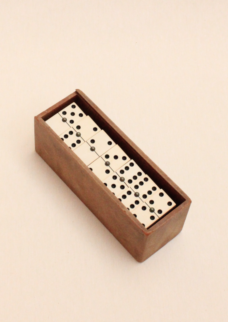 A wooden box containing a set of arranged Boga Avante Shop Dominoes, viewed from above on a light beige background.