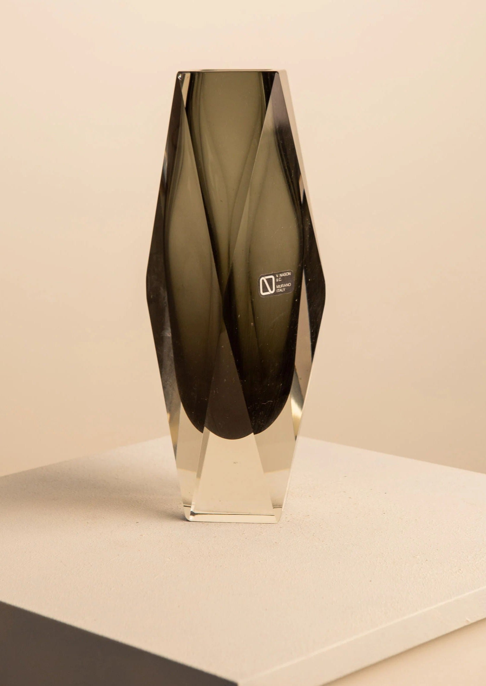 A sleek, transparent Treaptyque trophy crafted from blown glass with a dark, geometric design inside and a logo at the base, displayed on a light-colored pedestal against a neutral background.