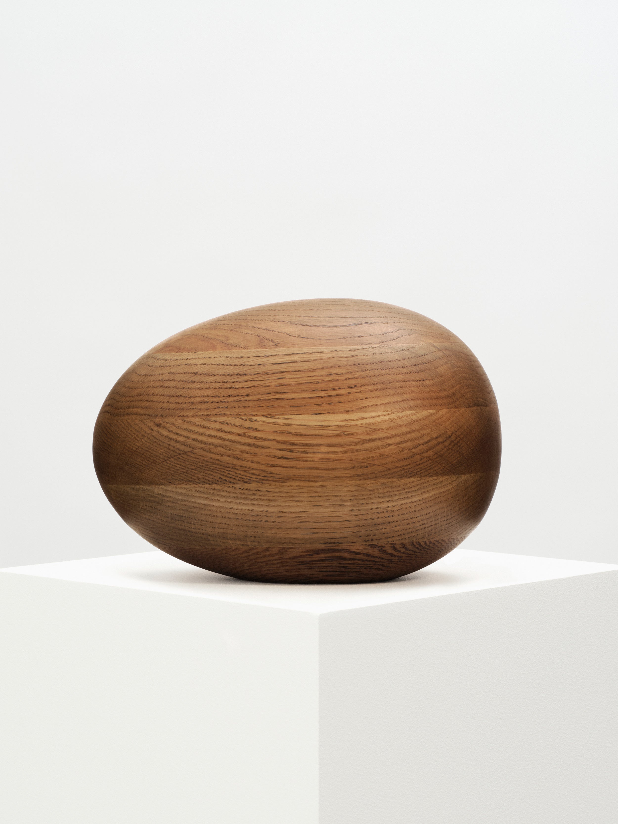 Smoked Oak Egg Sculpture resting on a wooden pedestal, showing intricate details and smooth texture