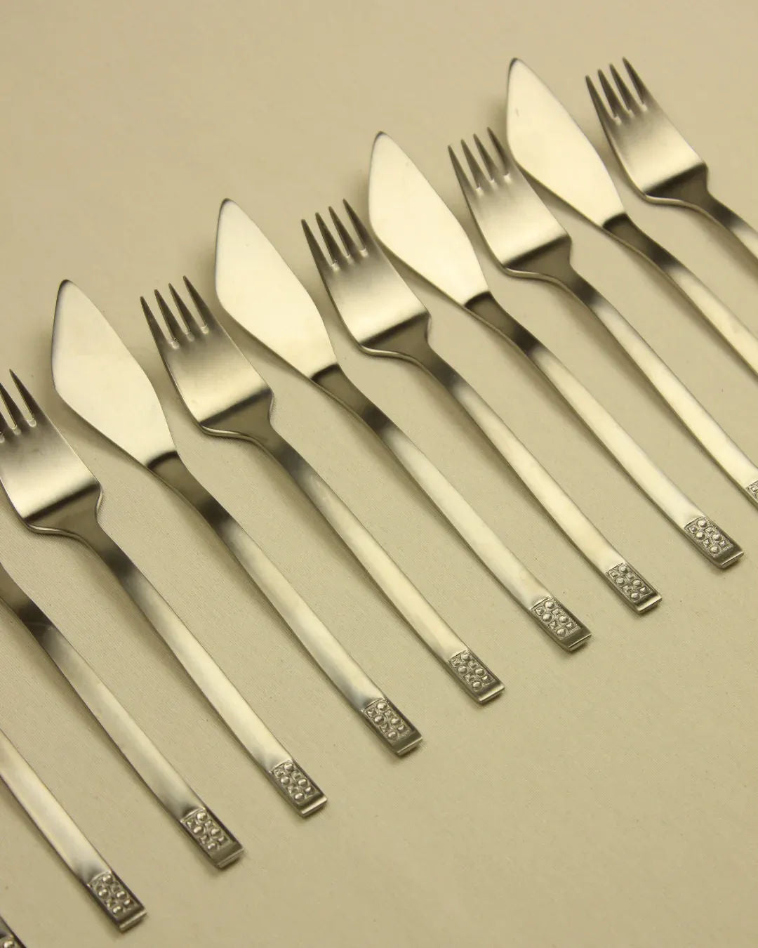 A symmetrical arrangement of Boga Avante Shop's Cutlery Set 70s Style in satin stainless steel forks and knives on a beige background, showcasing alternating patterns with handles aligned in a straight line.