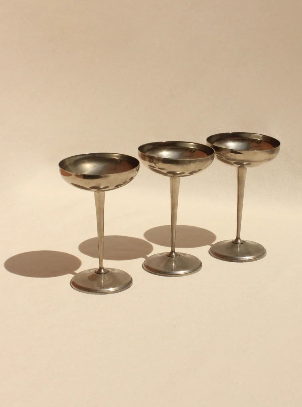 Three elegant Boga Avante Shop Alpaca Silver champagne coupes standing in a row on a neutral background with soft lighting casting gentle shadows.