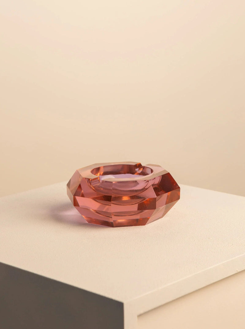 A translucent, peach-colored handcrafted Treaptyque 70's Murano glass ashtray with a faceted design, resting on a white pedestal against a soft beige background.
