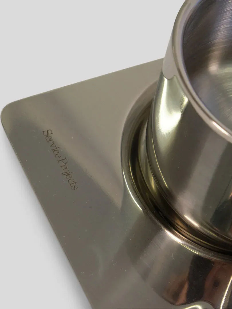 A close-up of a sleek stainless steel kitchen scale with a metallic bowl on top, angled to show the brand "Service Projects" engraved on the surface, reflecting an Italian design influence.