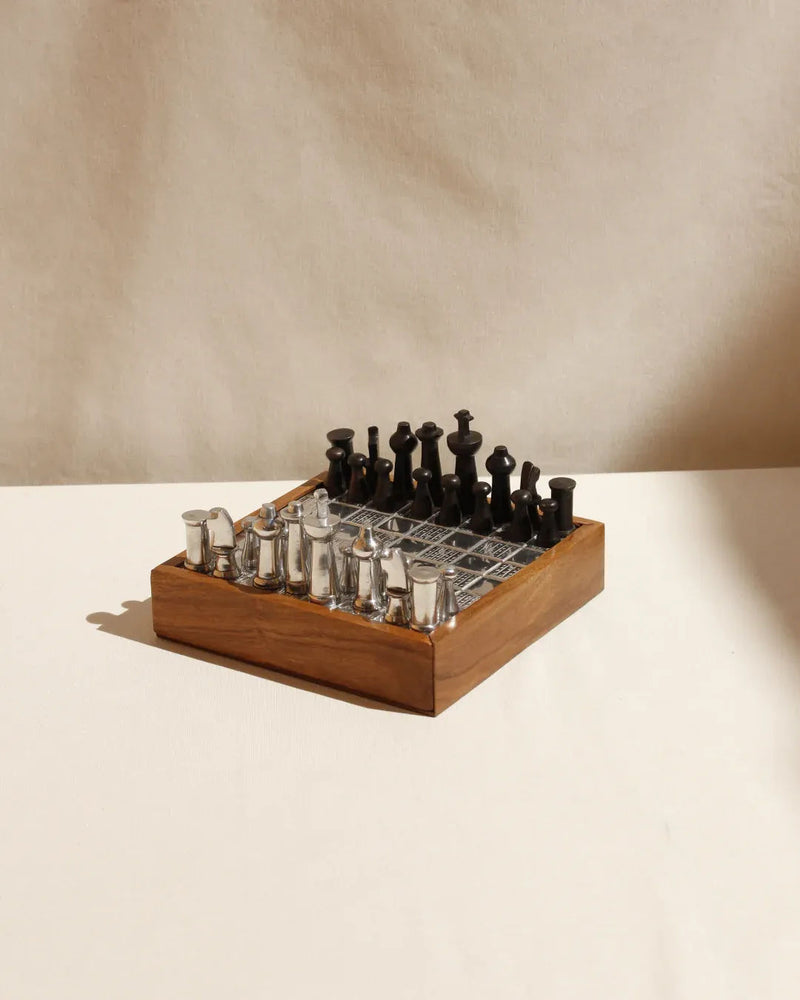 The Boga Avante Shop's Wood and Metal Chessboard is arranged for a match on a beige surface, blending contemporary design with black metal pieces. Viewed from an angle, the minimalist setup casts soft shadows, revealing a few elegant rows of this chic aesthetic.