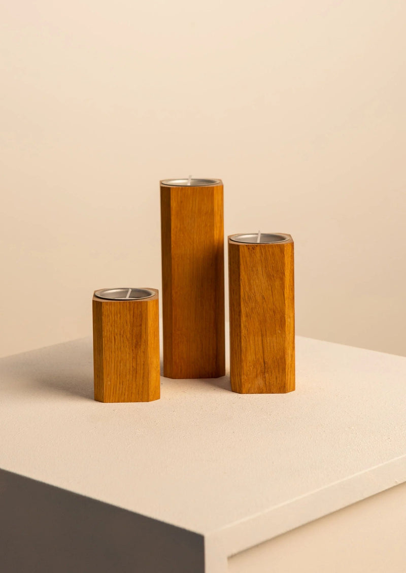Three cylindrical Treaptyque Oak Candleholders Set of varying heights with metallic interiors, staged on a gray surface against a cream backdrop.