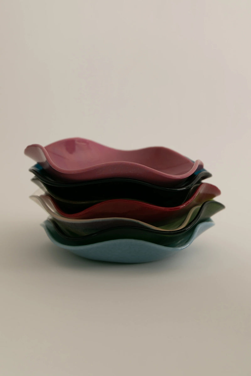 A stack of four large ceramic Sophie Lou Jacobsen Petal Plates in varying shades of deep red, burgundy, teal, and olive green on a pale background, showing a smooth and glossy finish.