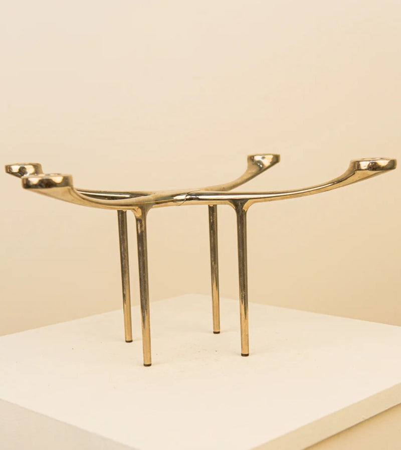 A minimalist sculpture of two elongated, golden arms extending upwards, each ending in a flat platform designed by Charles Wilson for Menu 00's, supported by slender, vertical poles on a light-colored base - Treaptyque Candelabra Chandelier.