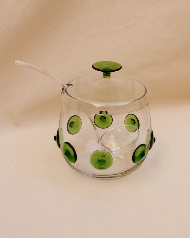 A handcrafted transparent glass Murano Punch Bowl with a matching lid, decorated with green circles and black outlines. The bowl has a spoon inserted through a notch in the lid. (Brand Name: Boga Avante Shop)