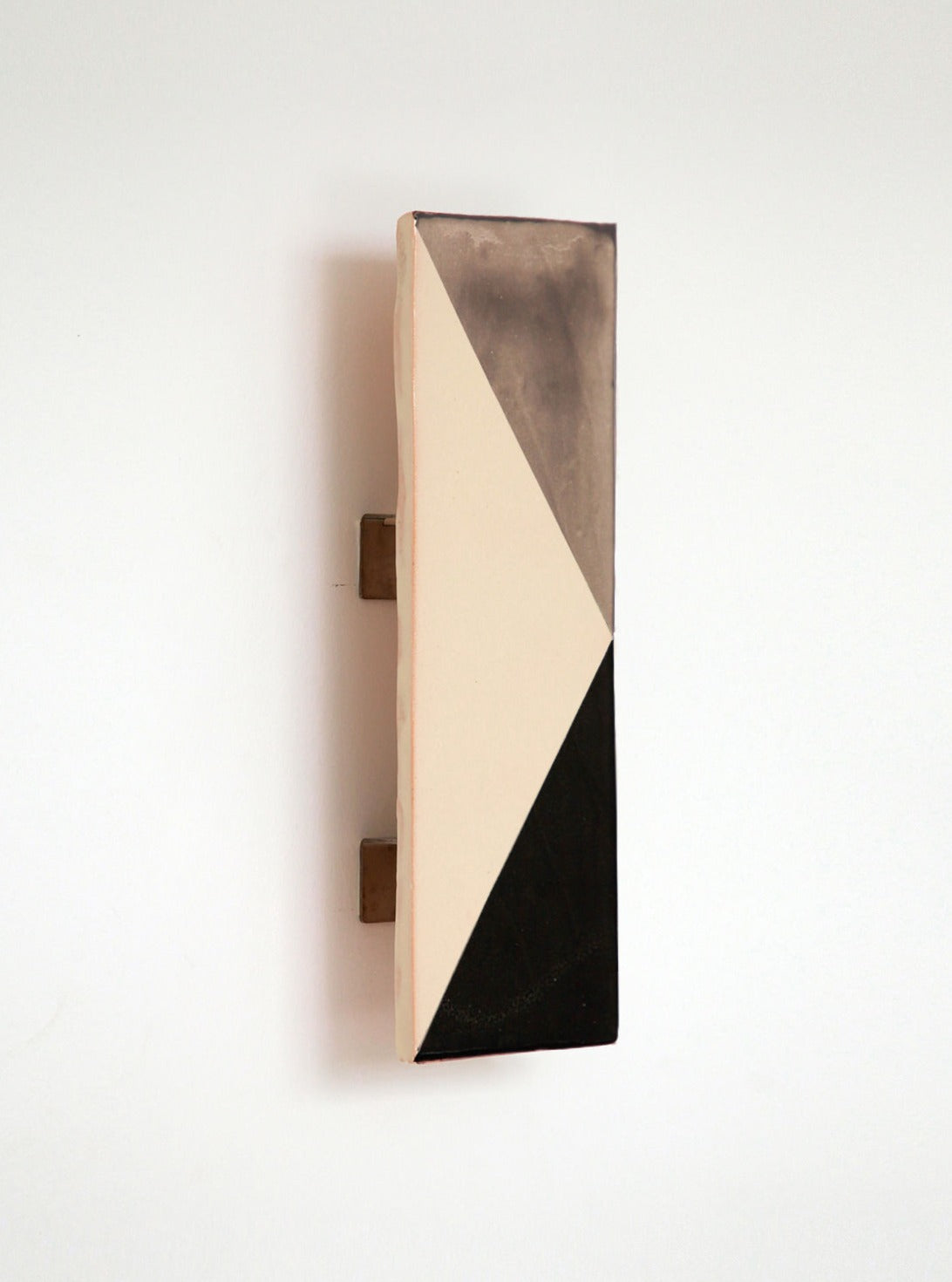 A minimalist light switch on a white wall, featuring an artisanal production design with a beige and black triangular pattern on its faceplate by Violaine d'Harcourt's Tile GN.