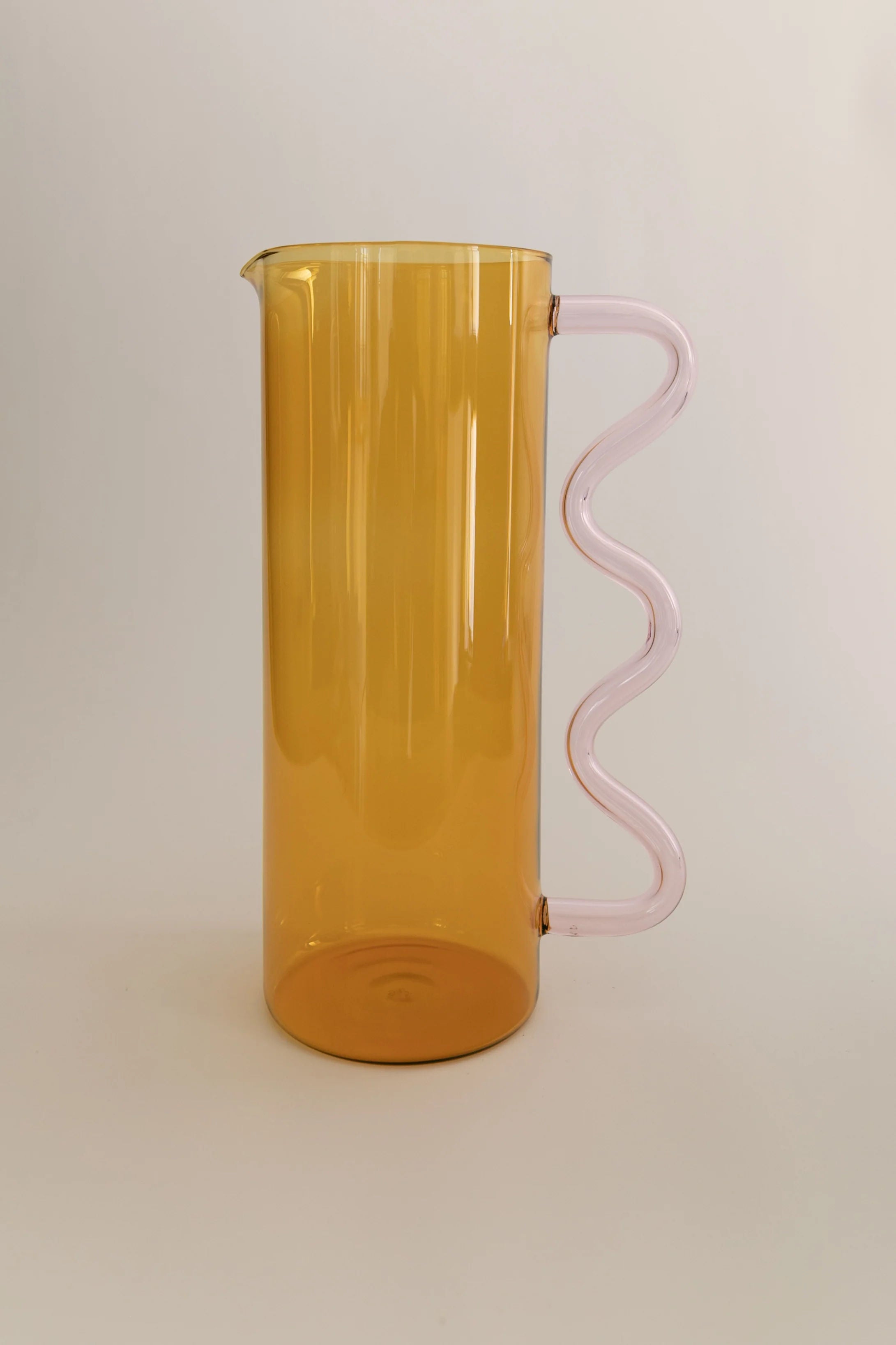 A tall, amber-colored borosilicate Wave Pitcher Glass pitcher with a unique pink spiral handle, positioned against a plain light background.