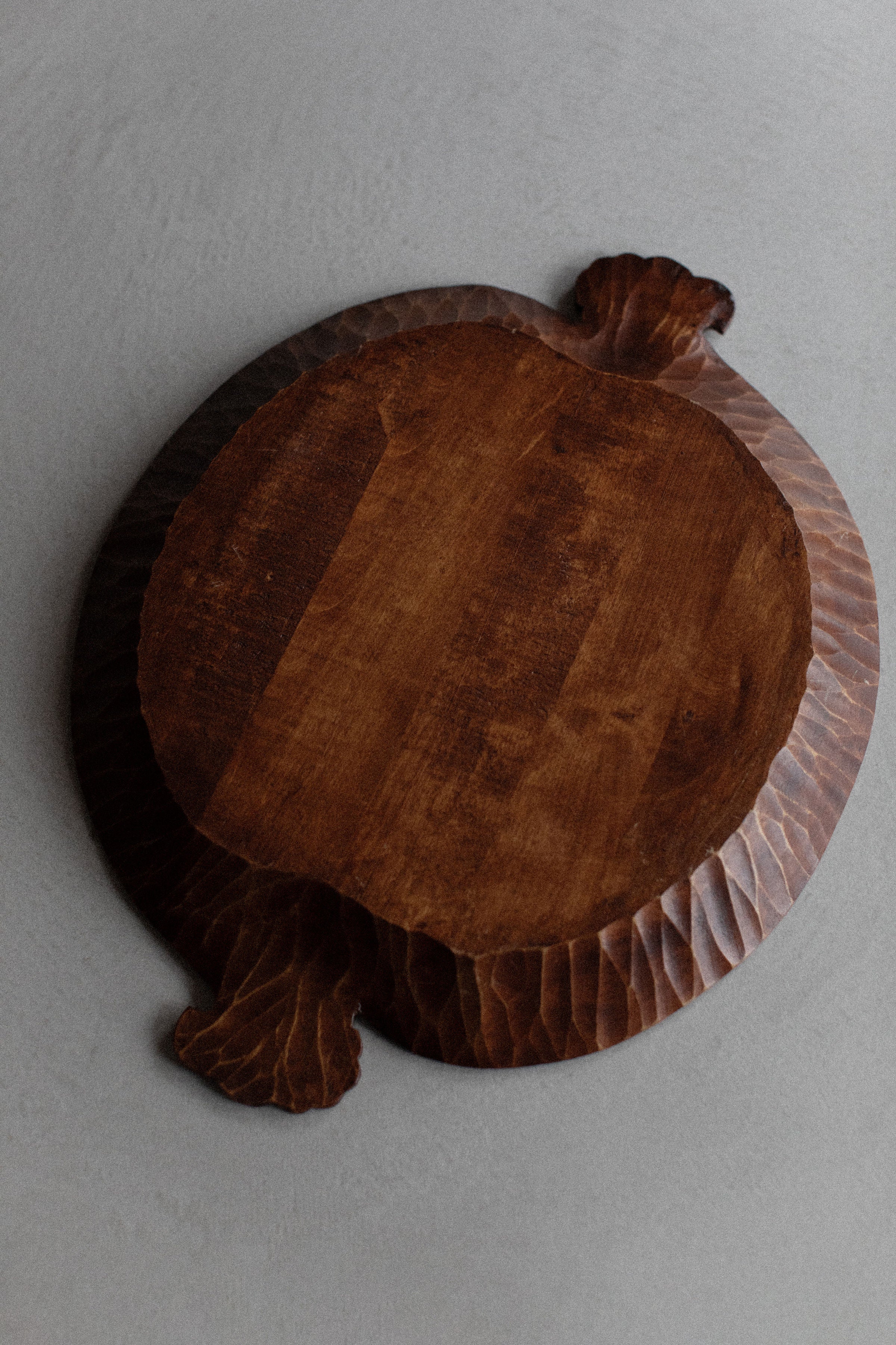 A Out For Lunch hand-carved wooden Art Deco Tray with a rustic, dark finish and textured edges that resemble leaf shapes, placed against a plain gray background.