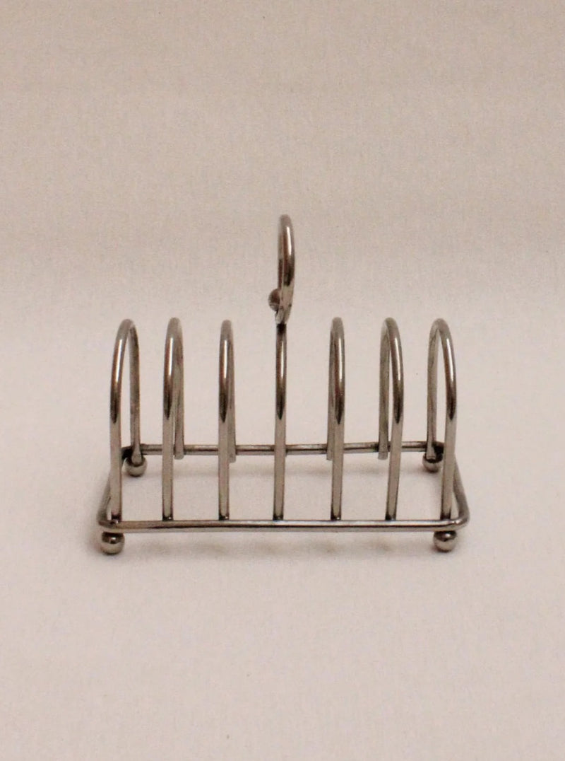 A Boga Avante Shop Art Deco Toast Rack with six slots, featured against a plain, light beige background. The rack has a central handle for carrying.