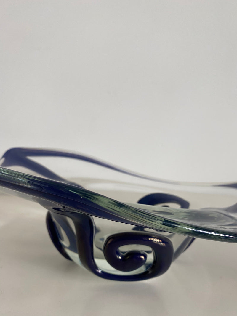 A Les Objets Amsterdam glass bowl with exquisite craftsmanship, featuring swirling blue accents and elegant curves, displayed against a plain white background.