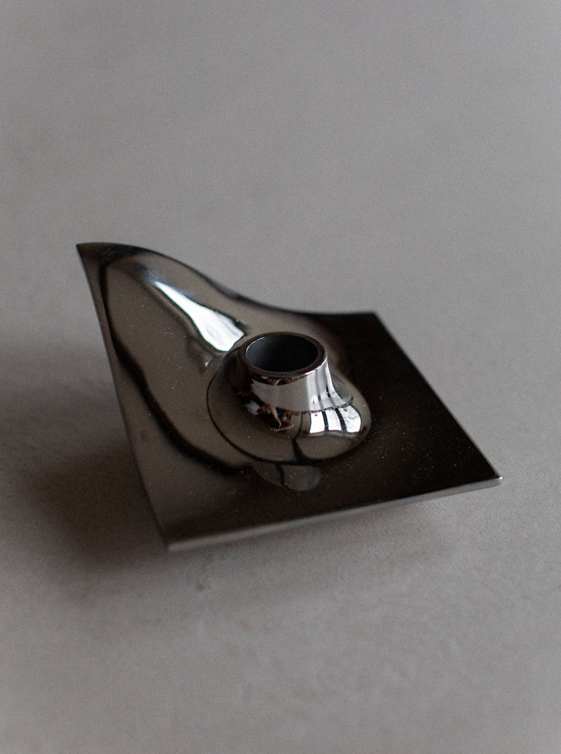 A metal ashtray with a reflective surface and a 70's Chrome Candle holder, sitting on a matte gray surface by Out For Lunch.